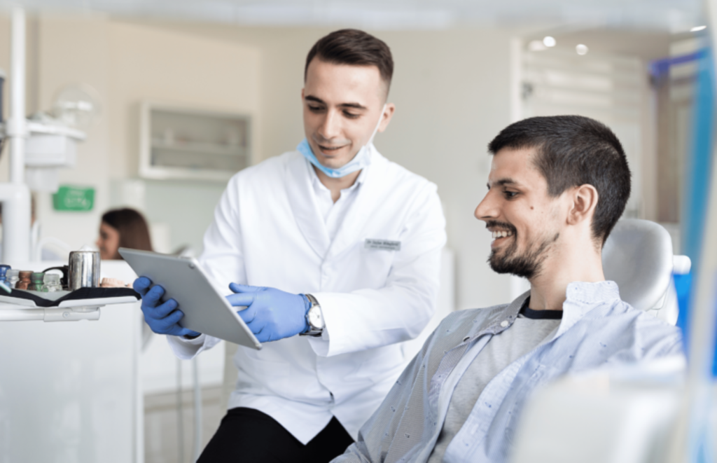 A dentist at a dentist's office holding a tablet is showing his patient the results