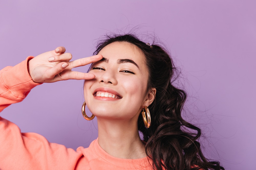 A stunning Asian female model with a beautiful smile showing a peace sign